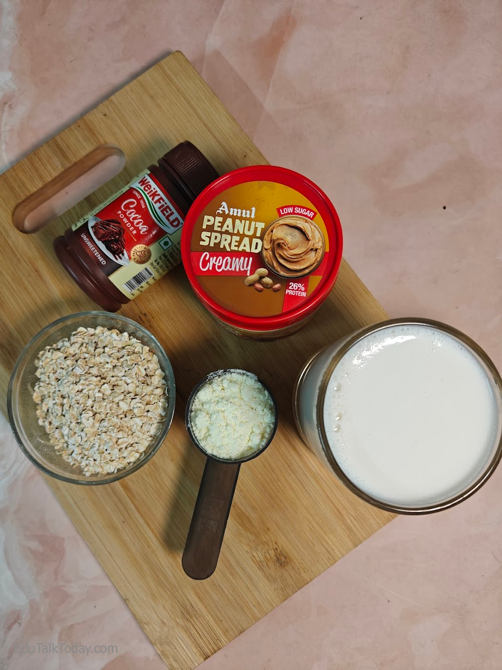 Ingredients for peanut butter oats smoothie including milk, oats, peanut butter, cocoa powder, and protein powder on a wooden board