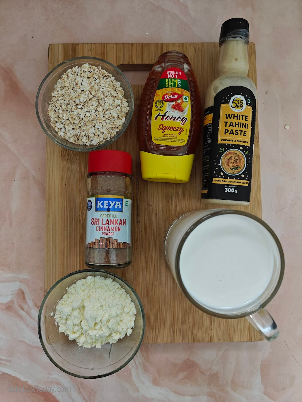 Ingredients Required To Make Oats Tahini Protein Smoothie laid out on a chopping board. 

Oats, Honey, White Tahini Paste, Milk, Protein Powder and Cinnamon